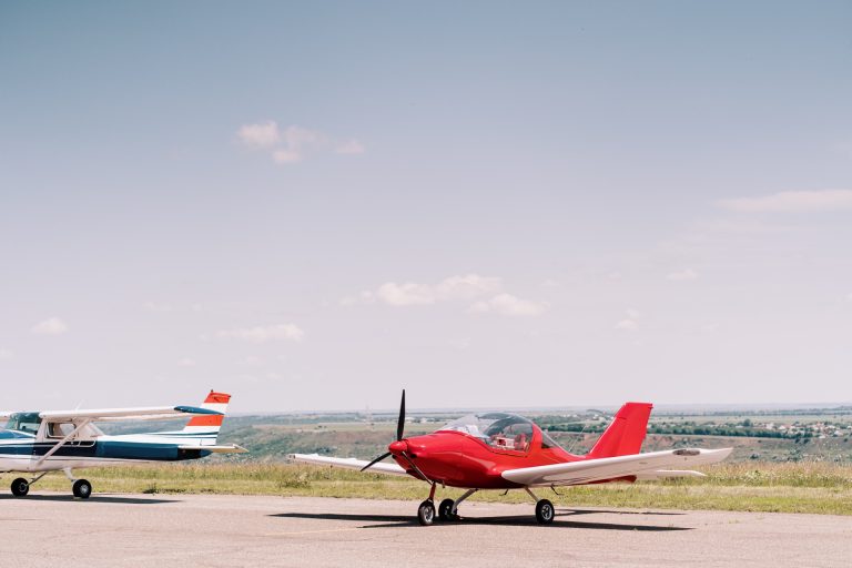 Två små privatflygplan, ett rött och ett blåvitt, på ett litet flygfält